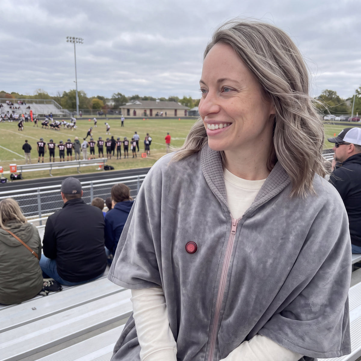 AI-generated illustrative casual football-game photo of a woman wearing the Grey CozyCovers cape