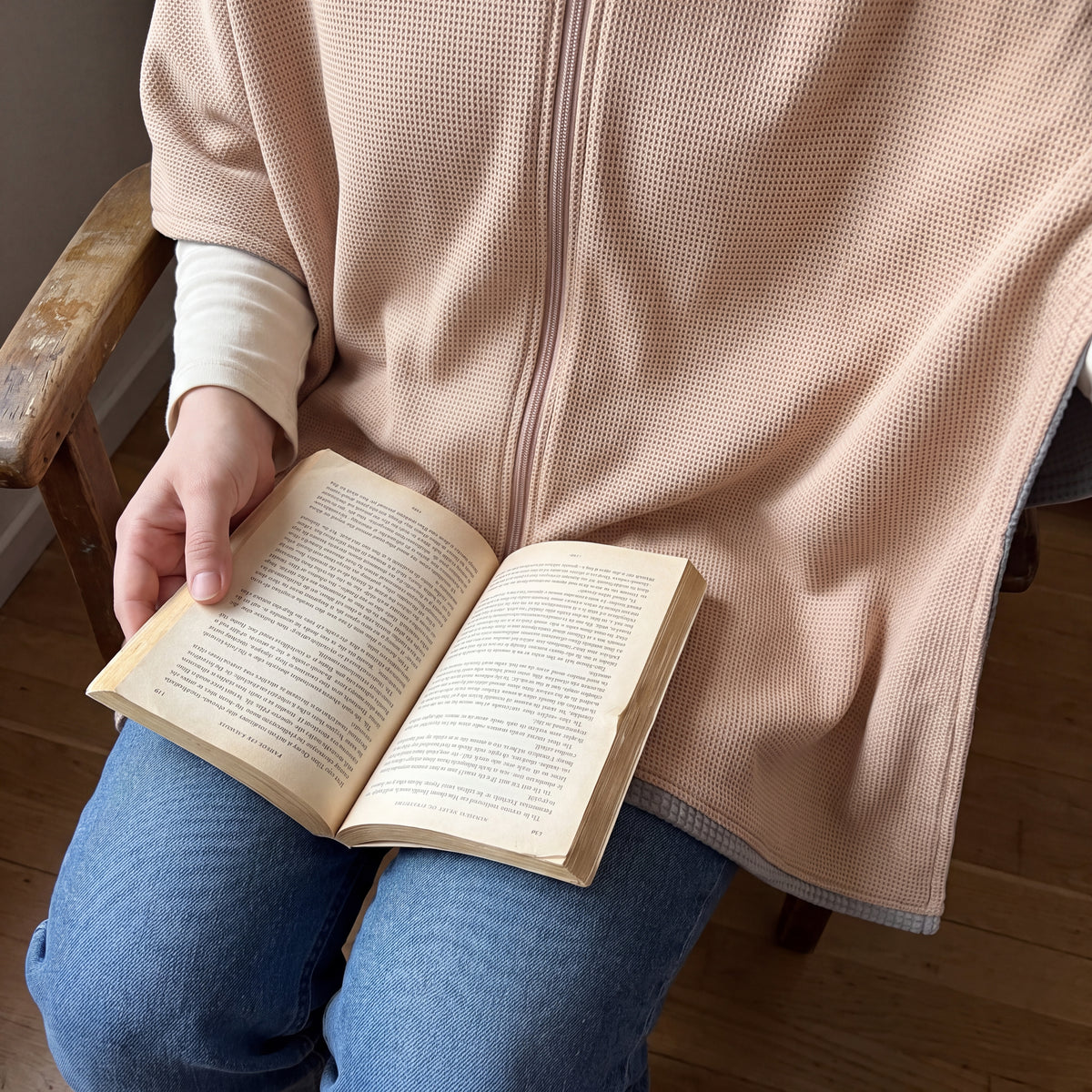 AI-generated illustrative close-up of an open book on a reader's lap with the Apricot CozyCovers cape and center zip